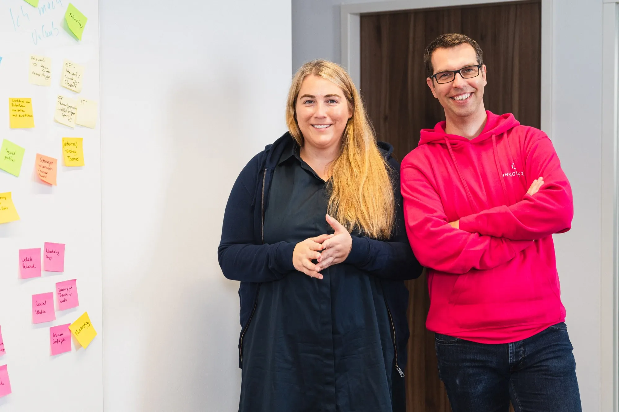 Julia and Matthias in front of a wall of sticky notes from a workshop