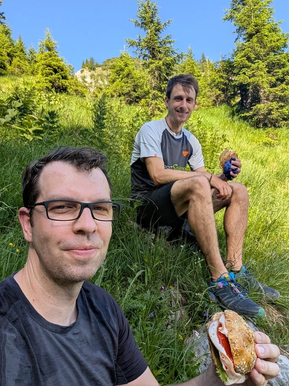 Two colleagues having a snack on a meadow during a mountain hike